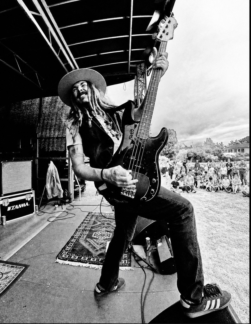 Bassist med hatt spiller mot publikum i gresset